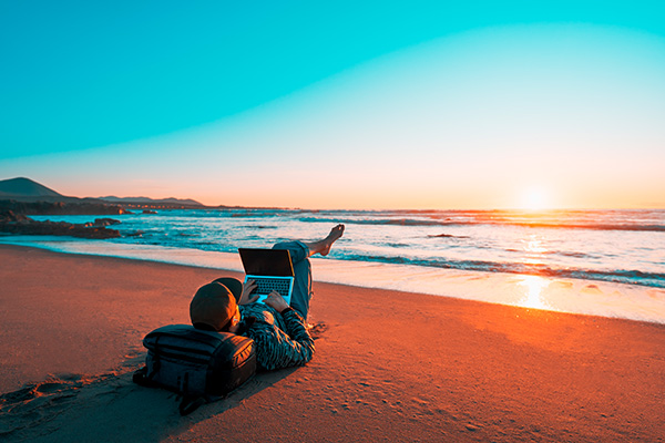 Nómada digital trabajando con una laptop en una playa al atardecer