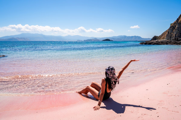 Mujer turista sentada en la arena rosada de Pink Beach, Indonesia. con el mar azul de fondo en un día soleado.