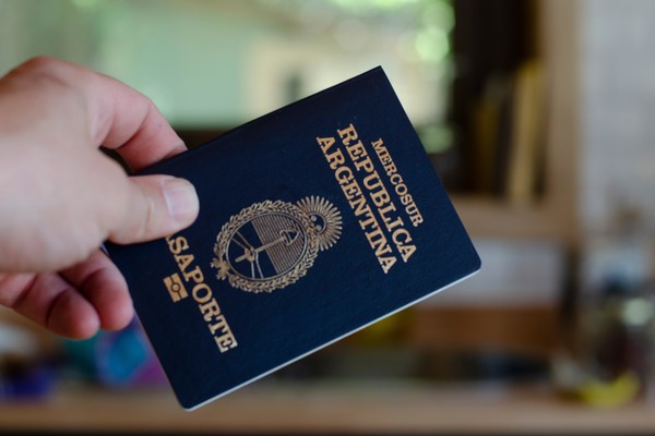Primer plano de una mano sosteniendo pasaporte argentino azul con un fondo borroso.