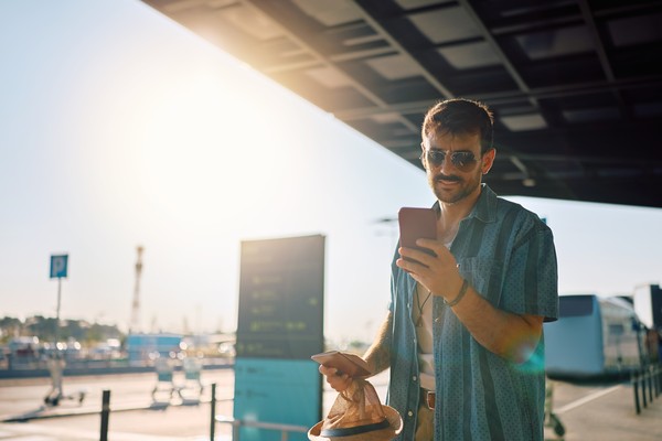 Viajero masculino usando un smartphone en los alrededores del aeropuerto.