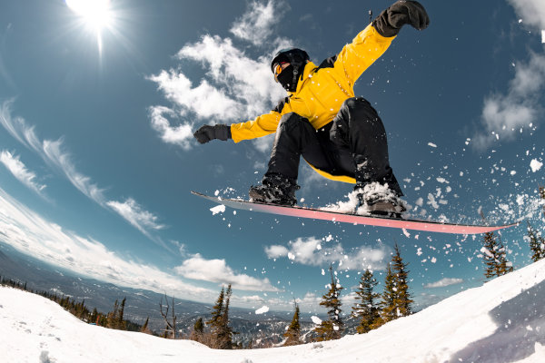 Joven masculino realizando un salto en una tabla de snowboard sobre la nieve en un día soleado.
