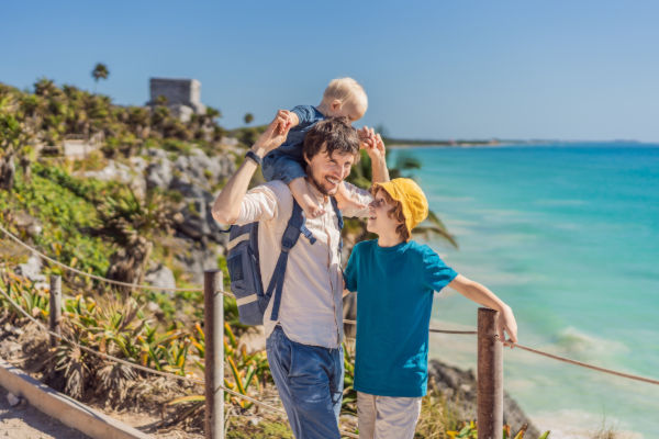 Padre con sus hijos caminando junto al mar en la zona arqueológica de Tulum.