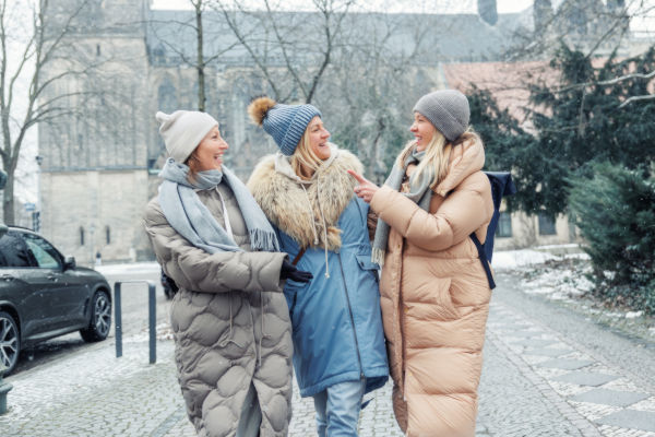Mujeres caminando por una ciudad alemana en invierno, abrigadas con camperas y gorros.
