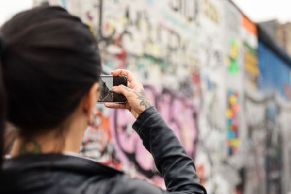 Turista fotografiando una sección del Muro de Berlín cubierta de grafitis coloridos.