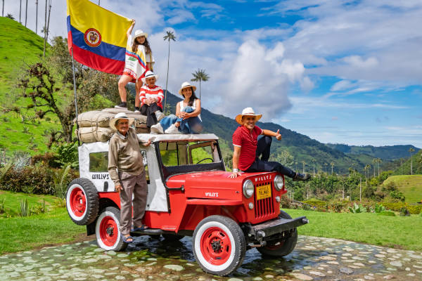 Grupo de turistas y lugareños en jeep rojo clásico con la bandera nacional de Colombia recorriendo el Valle del Cocora.