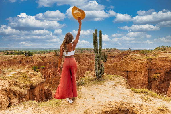 Mujer turista en el borde de un risco alzando el brazo junto a un cactus en el desierto de Tatacoa, la segunda zona árida más grande de Colombia.