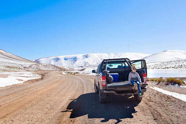 Niño pequeño sentado en la parte trasera de una camioneta tipo pick-up estacionada en una calle de tierra en el desierto de Atacama, Chile.