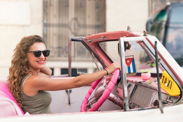 Mujer turista sonriente en un auto clásico cubano sin techo.