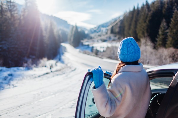 Vista posterior de la mujer viajera admirando las montañas nevadas desde su auto detenido con la puerta abierta.