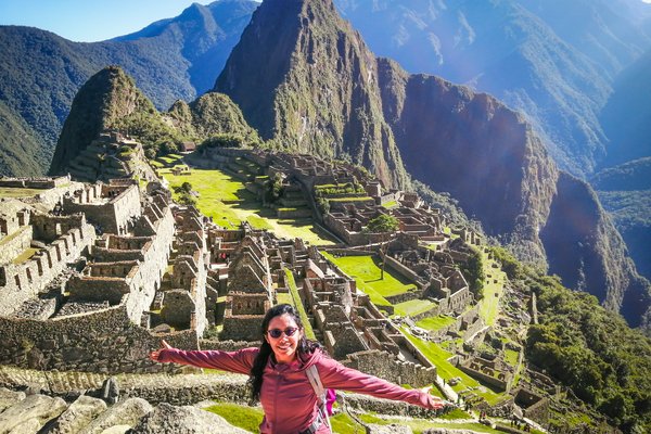 Turista feliz posando para una foto en el Santuario Histórico de Machu Picchu, ciudadela inca ubicada en lo alto de la Cordillera de los Andes, en Perú.