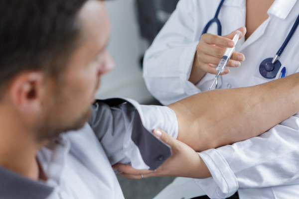 Profesional de la salud con bata y estetoscopio colocando vacuna en el brazo de hombre de mediana edad.