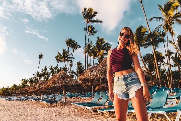 Mujer joven sonriente en la playa Bávaro, Punta Cana, República Dominicana, con reposeras y palmeras de fondo al atardecer