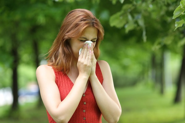 Mujer joven sonándose la nariz en un parque.
