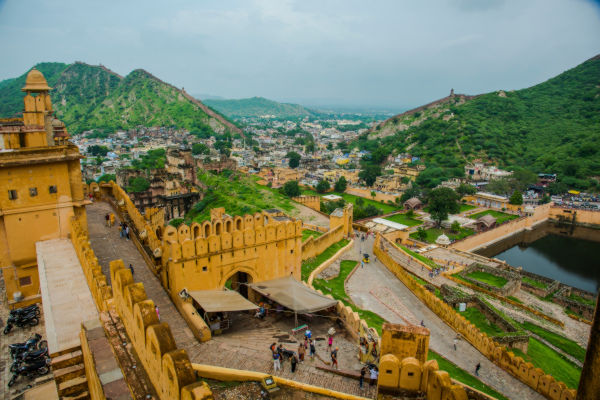Vista panorámica del Fuerte Amber en Jaipur, India, con colinas verdes de fondo y turistas recorriendo el lugar.