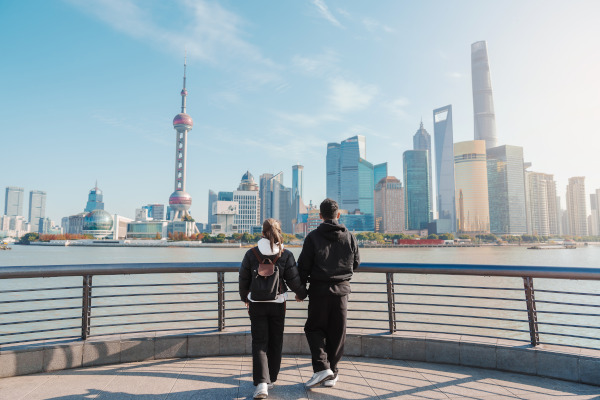 Pareja de turistas con mochilas observando el paisaje urbano de Lujiazui en el Bund de Shanghai.