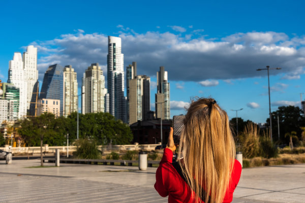 Mujer turista tomando fotografía con el teléfono móvil de unos edificios en Puerto Madero, Buenos Aires, en un día parcialmente nublado