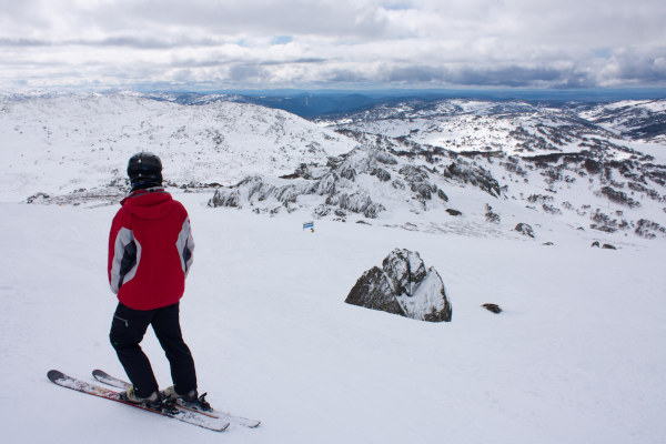 Esquiador en lo alto de una pista de esquí en Perisher, Australia, mirando hacia los picos nevados cercanos.