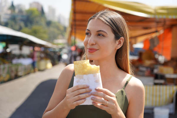 mujer turista comiendo un pastel en una feria de Brasil.