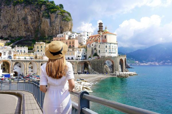 Mujer de espaldas sobre una barandilla viendo la pequeña playa de Atrani, Costa Amalfitana, Italia.