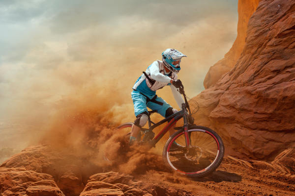 Ciclista con casco conduciendo una bicicleta de montaña en tierra rojiza y polvorienta.