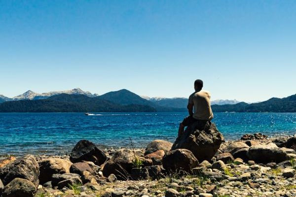 joven sentado en una roca contemplando el paisaje de lagos y montañas en las orillas del Lago Nahuel Huapi.