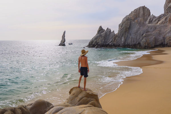 Hombre parado en una roca en la Playa del Amor en Cabo San Lucas.