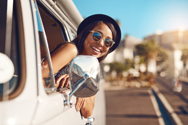 Mujer turista asomando por la ventanilla de una furgoneta en una carretera durante un viaje en un día soleado