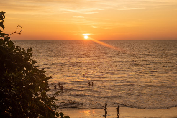 Atardecer en Playa Ladrilleros, Buenaventura, Colombia, con personas todavía en el agua y caminando por la orilla.