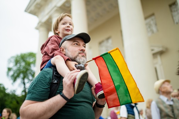 Padre llevando a su hijo en hombros con una bandera de Lituania en la mano.