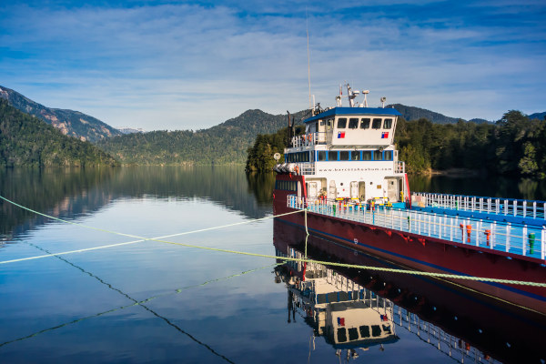 Ferry en el lago Pirehueico con montañas verdes de fondo en un día soleado, Puerto Fuy, Chile.