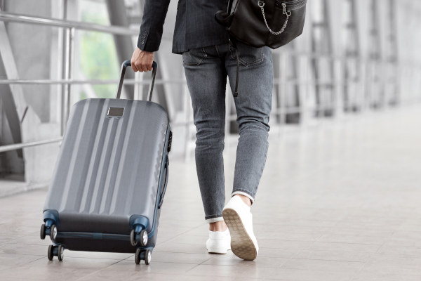 Hombre de espaldas llevando maleta gris por un aeropuerto irreconocible.