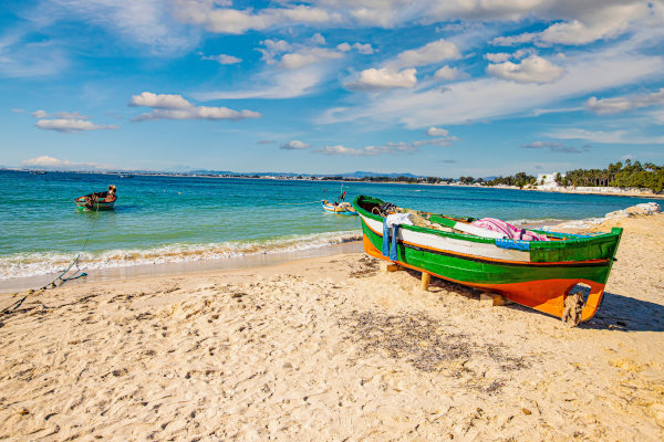 Bote colorido en la arena de una playa de Hammamet, Túnez, en un día soleado con mar azul de fondo.