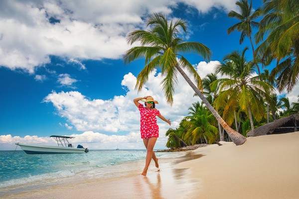 Mujer feliz disfrutando de la playa en isla de Saona, República Dominicana, con palmera y lancha de fondo