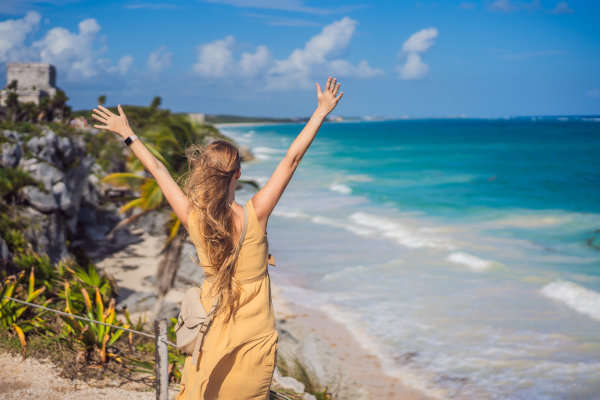 Mujer turista con los brazos alzados frente a una playa de la ciudad amurallada de Tulum, Riviera Maya, México.