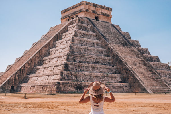 Mujer turista con sombrero de espaldas mirando la Pirámide de Kukulkán en Chichen Itzá, México