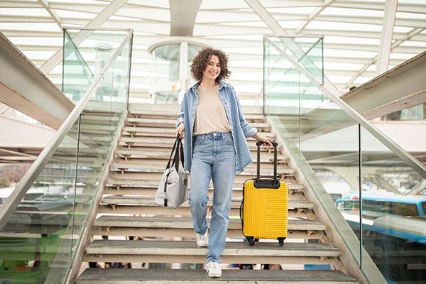 Viajera en escaleras de un aeropuerto con maleta y bolso de mano
