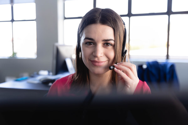 Personal femenino de atención al cliente mirando a cámara con una leve sonrisa mientras sostiene auricular con micrófono cerca de su mejilla.