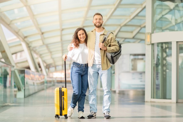 Pareja de viajeros posando para la foto en el aeropuerto con mochilas y maletas.