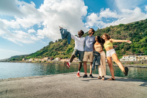 Grupo de amigos abrazados celebrando en un muelle costero durante sus vacaciones de verano en un día soleado.