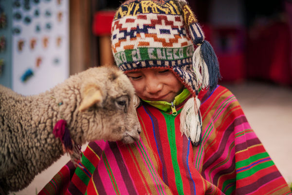 Niño peruano en la zona de Cusco, vestido con poncho y gorro, acompañado por una pequeña oveja.