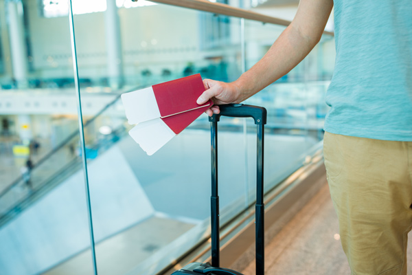 viajero sosteniendo pasajes en el aeropuerto junto a una maleta