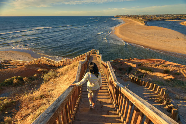 Mujer turista caminando por el icónico paseo marítimo de Port Noarlunga mientras ve la puesta de sol, Australia del Sur