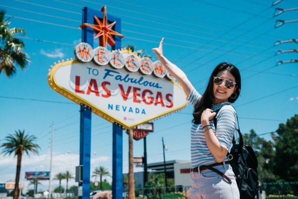 Mujer turista feliz bajo el cartel de bienvenida a Las Vegas, Nevada, en un día soleado