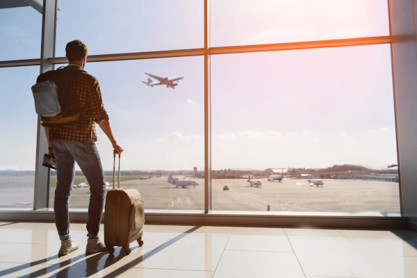 Turista masculino en aeropuerto con equipaje, viendo un avión por la ventana
