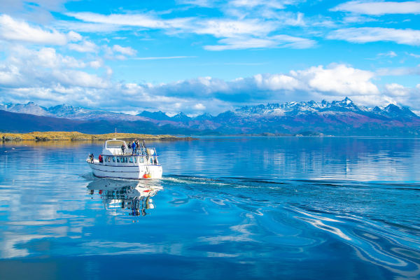 Embarcación navegando por el Canal de Beagle con montañas nevadas al fondo y aguas calmas en Ushuaia, Argentina.