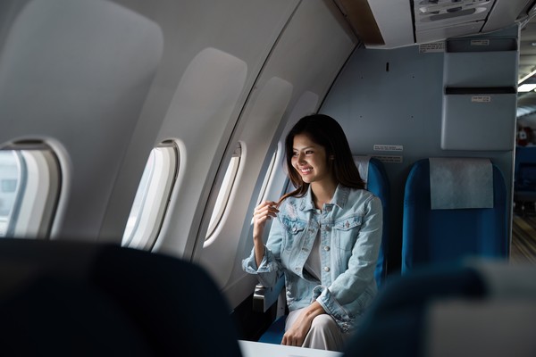 Mujer sentada en avión del lado de la ventanilla disfrutando del paisaje a través de esta mientras se toca el cabello.