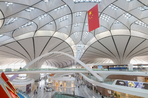 Interior del Aeropuerto de Daxing con techos con tragaluces visibles y una bandera de la República Popular China colgando en lo alto.