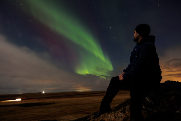 Hombre sentado observando una aurora boreal en el cielo nocturno.