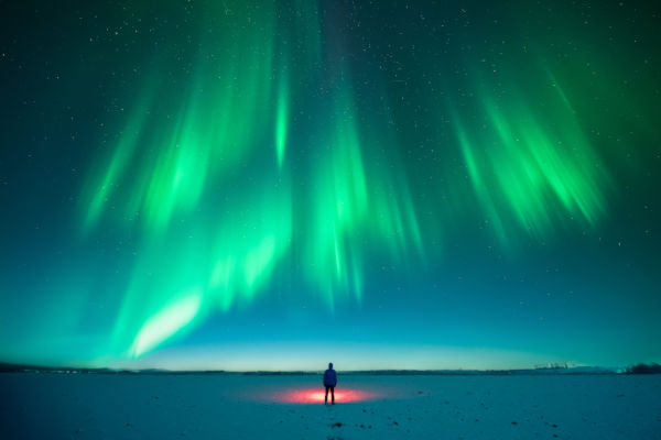 Persona bajo una aurora boreal en un paisaje nevado.