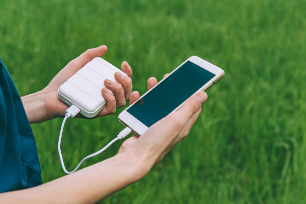 Persona sosteniendo celular apagado en una mano y una batería externa tipo power bank en la otra, ambos conectados mientras cable USB.